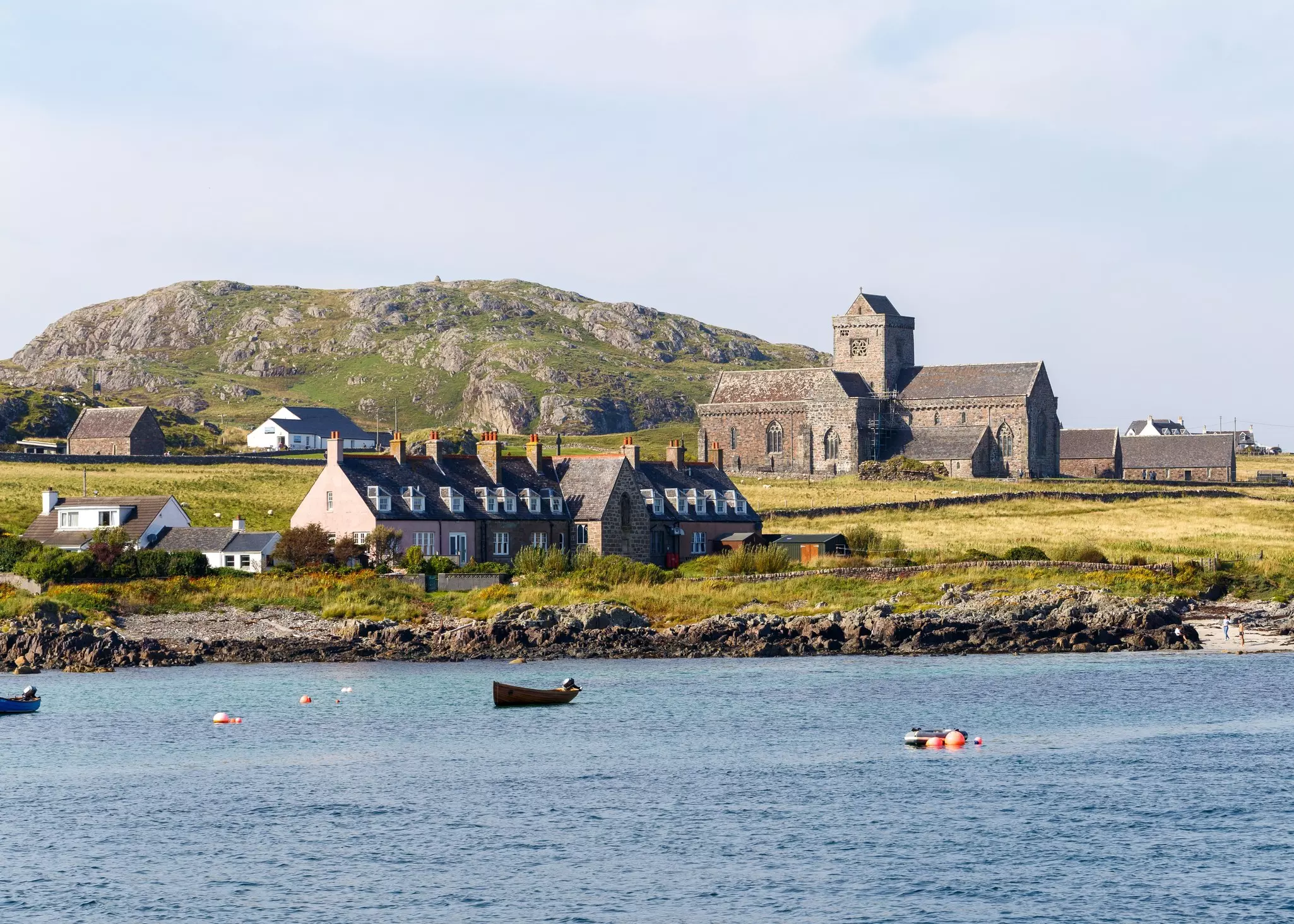 A row of stone cottages stand nearby an ancient abbey near the water's edge on a remote island. 