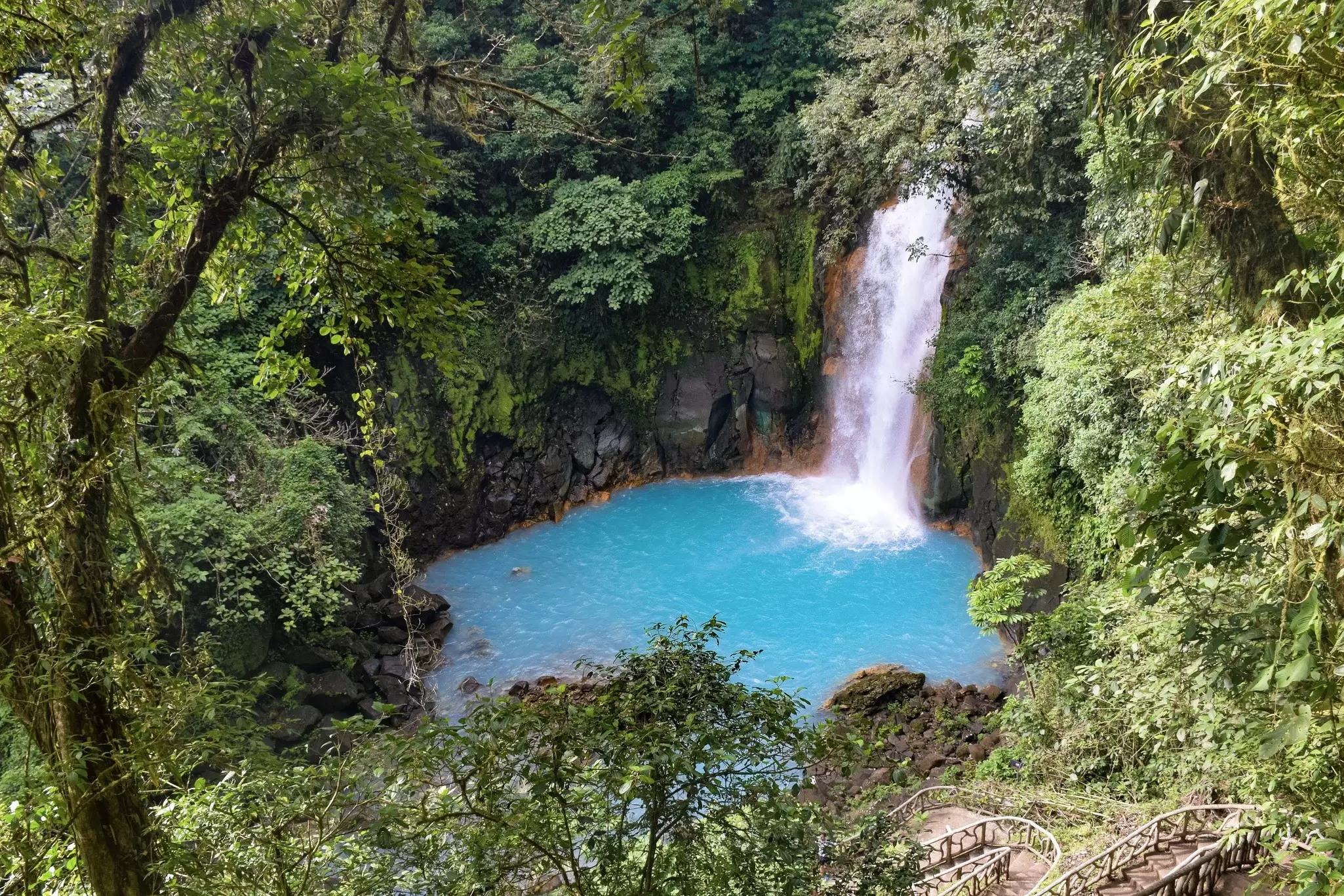 A waterfall cascades into a turquoise pool surrounded by green trees.