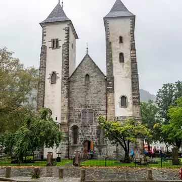 Romanesque stone church with two white-plastered towers and grey pyramid roofs above a cobbled street, overcast sky