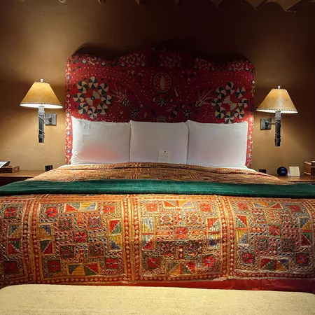 A bed with a patterned spread, three white pillows and lit sconces on either side.