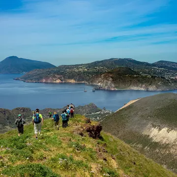 A group of hikers walk through a mountain meadow heading down towards the coastline.
