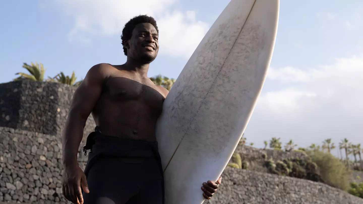 Man holding a long surf board on a beach in Tenerife, Canary Islands, Spain