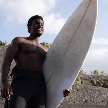 Man holding a long surf board on a beach in Tenerife, Canary Islands, Spain
