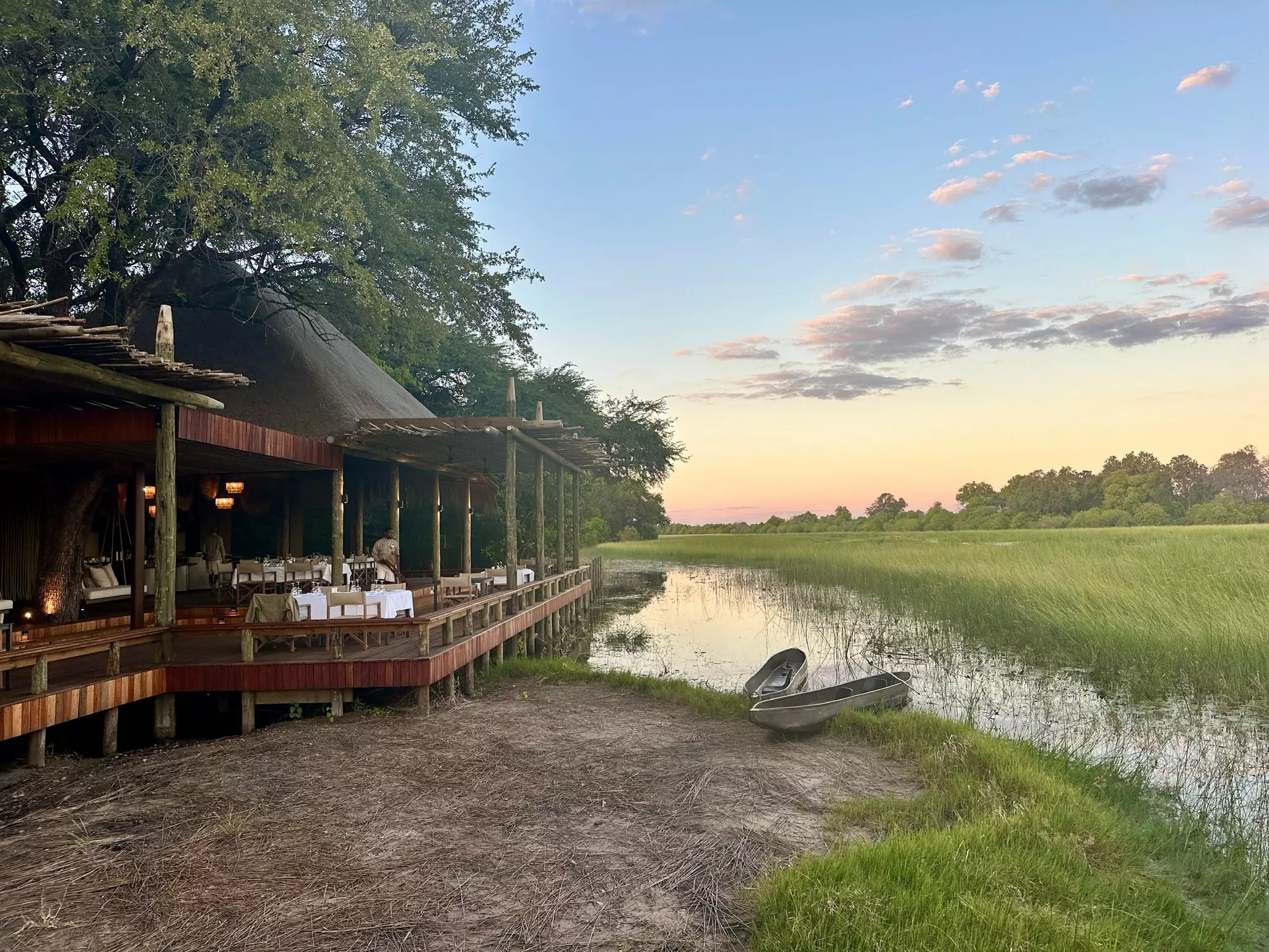 Sediba Sa Rona lodge in Botswana with two boats on the edge of the water and an open field at sunset