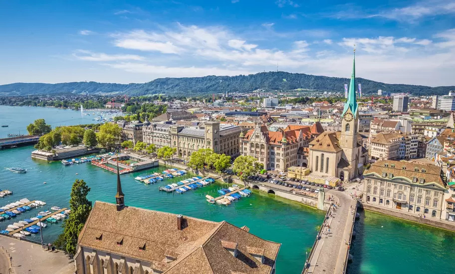 An aerial view of historic Zurich city centre on a sunny day with the famous Fraumunster Church and river Limmat in the foreground.
