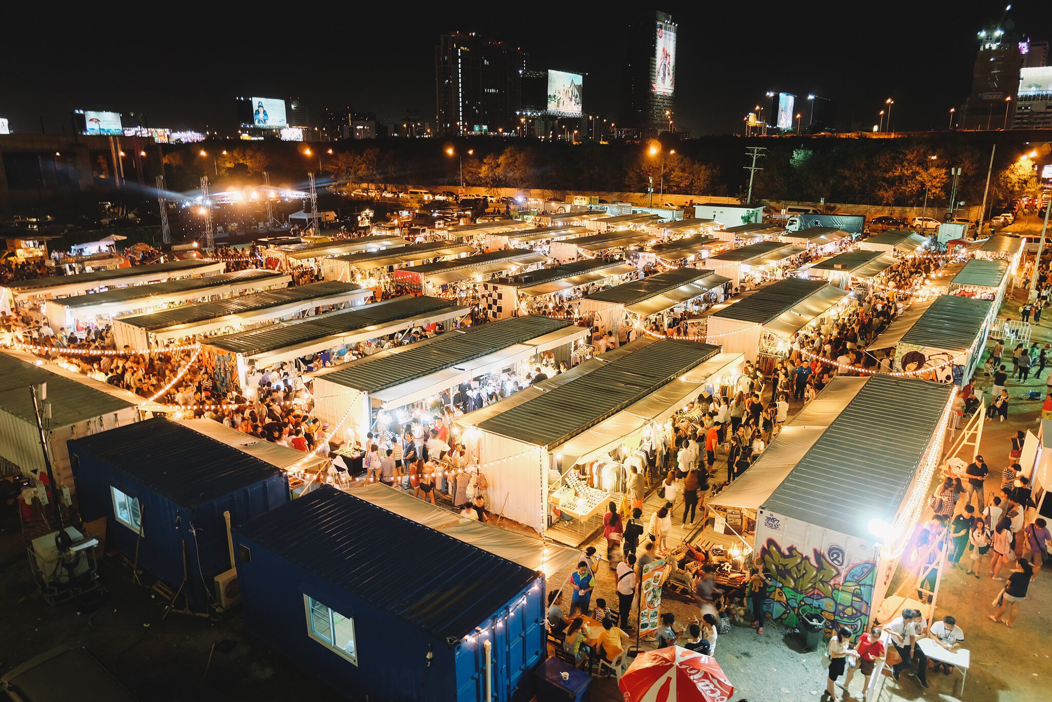 From an aerial view, the stalls of a night market glow with light as vendors sell their wares.