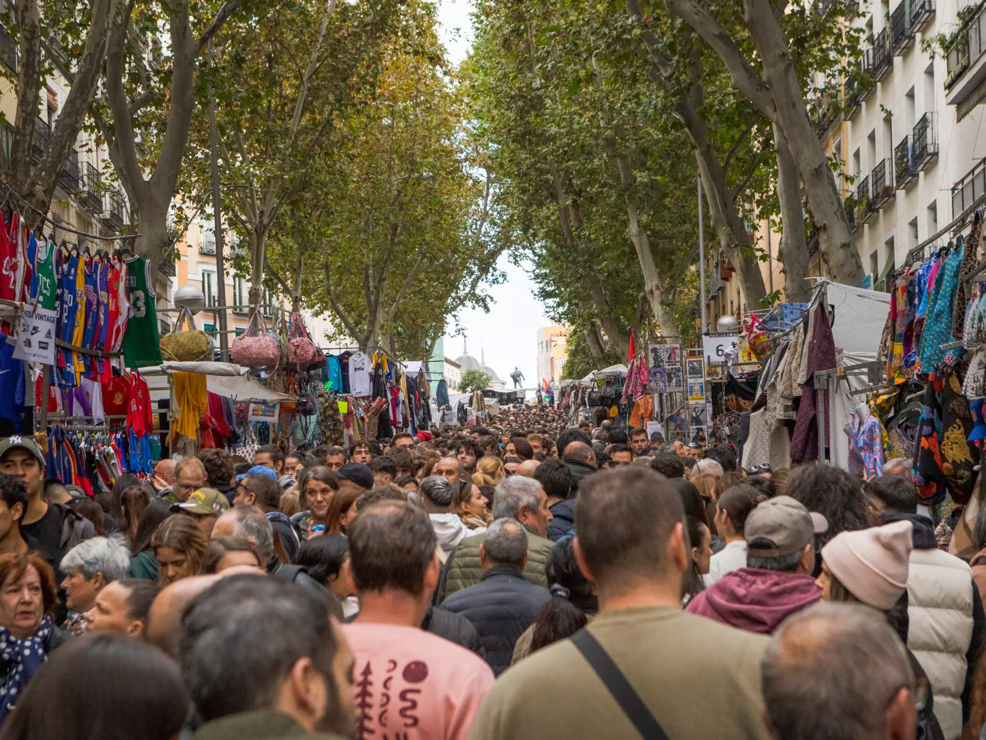 A dense crowd of people at a market in a street in a city.