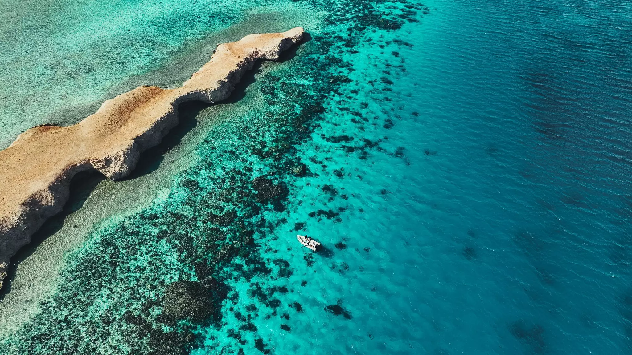 A boat floats by a rocky outcrop in the clear blue waters of the Red Sea off Saudi Arabia.