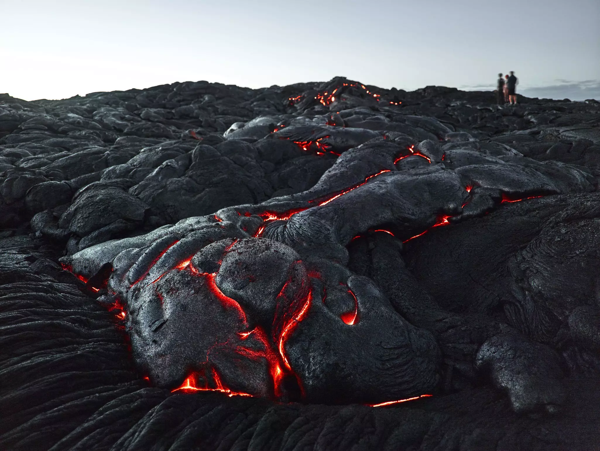Visitors standing on a glowing lava field on an overcast day.