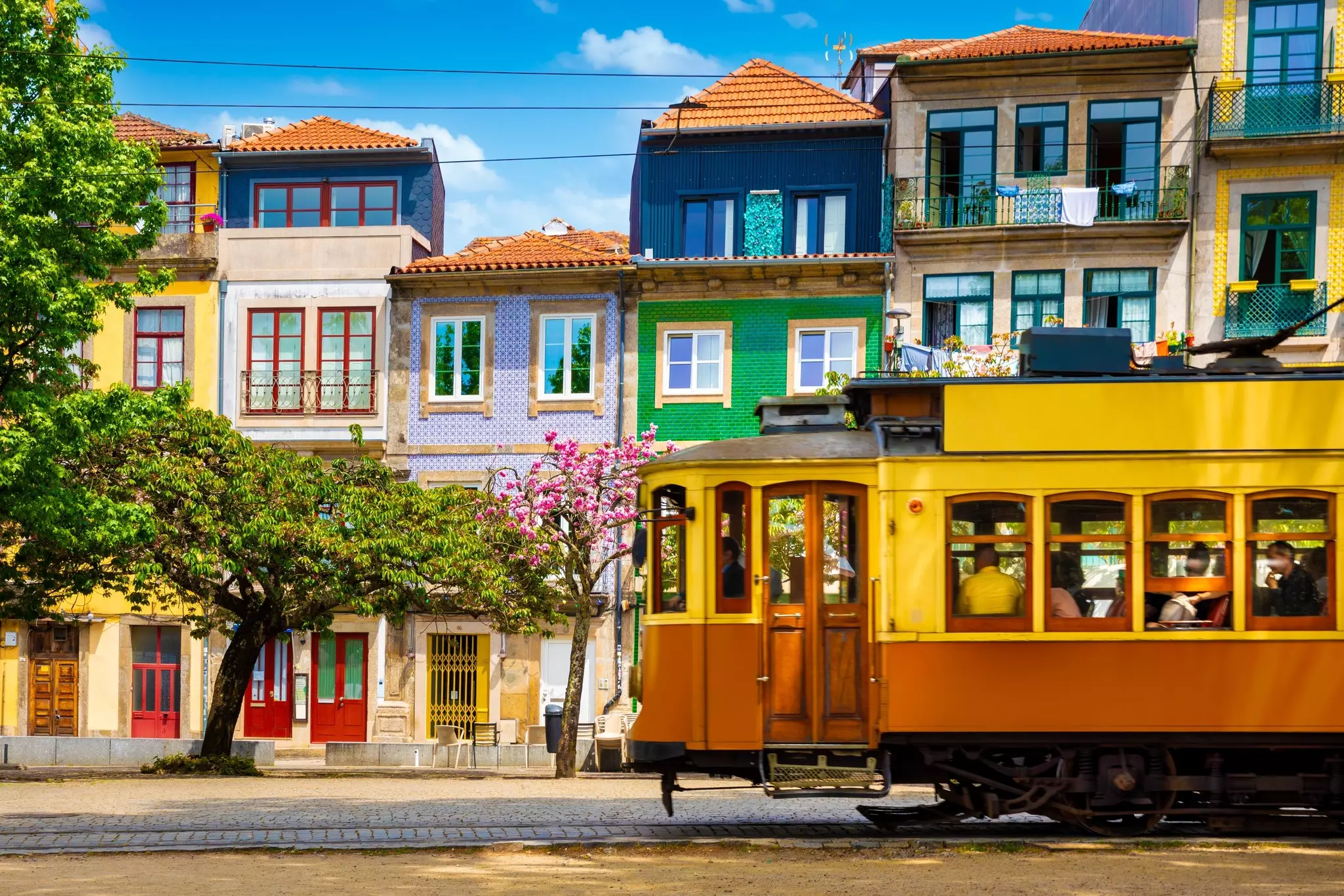 A traditional tram passes a row of colorful houses bathed in sunshine on a summer's day.