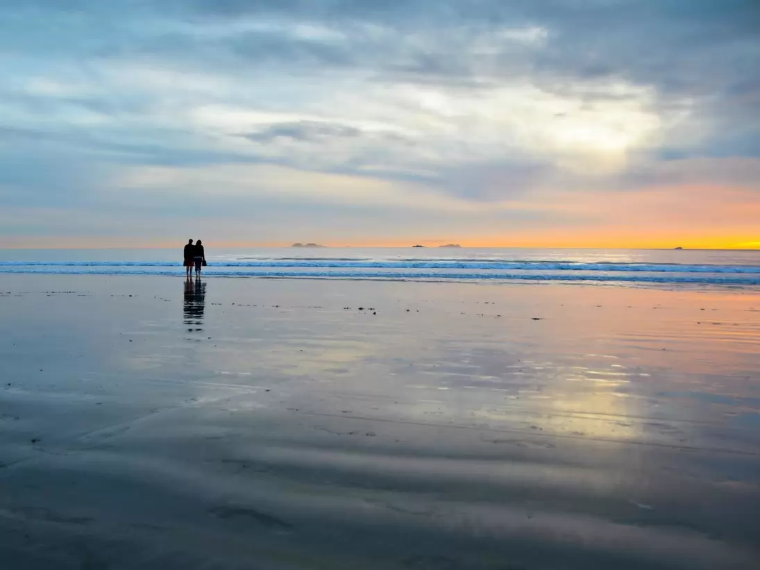 2E5BKXB Young couple silhouettes on the Silver Strand Beach wet sand  watching the sunset at Coronado Island, San Diego Southern California USA.