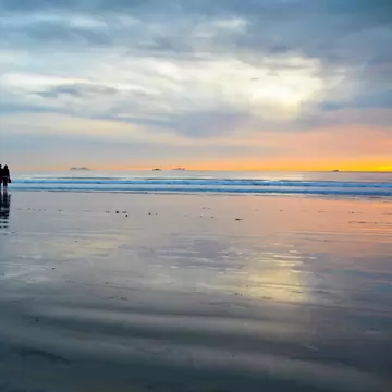2E5BKXB Young couple silhouettes on the Silver Strand Beach wet sand  watching the sunset at Coronado Island, San Diego Southern California USA.