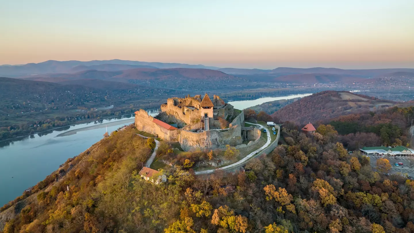 Aerial panoramic drone view of the beautiful high castle of Visegrad on a moody autumn sunset along the Danube Bend (Dunakanyar) and amazing golden sunset at background.