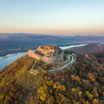 Aerial panoramic drone view of the beautiful high castle of Visegrad on a moody autumn sunset along the Danube Bend (Dunakanyar) and amazing golden sunset at background.