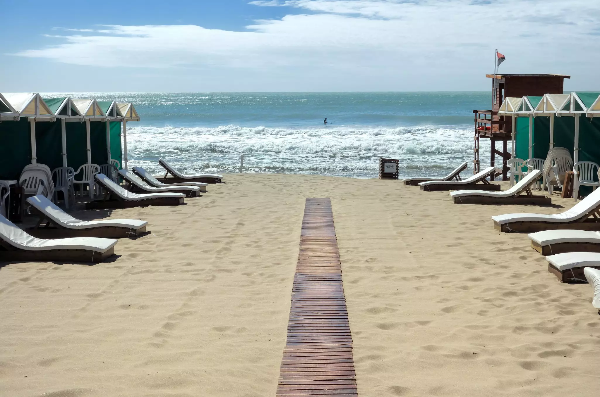 A wooden boardwalk passes beach shelters and lounges at Mar del Plata during the early morning.
