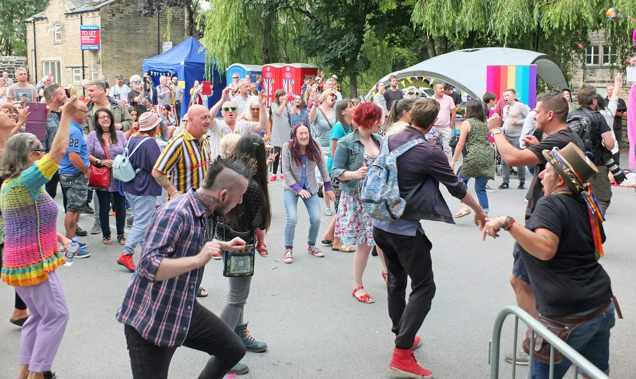People of all ages dancing in the street at a party in a small town.