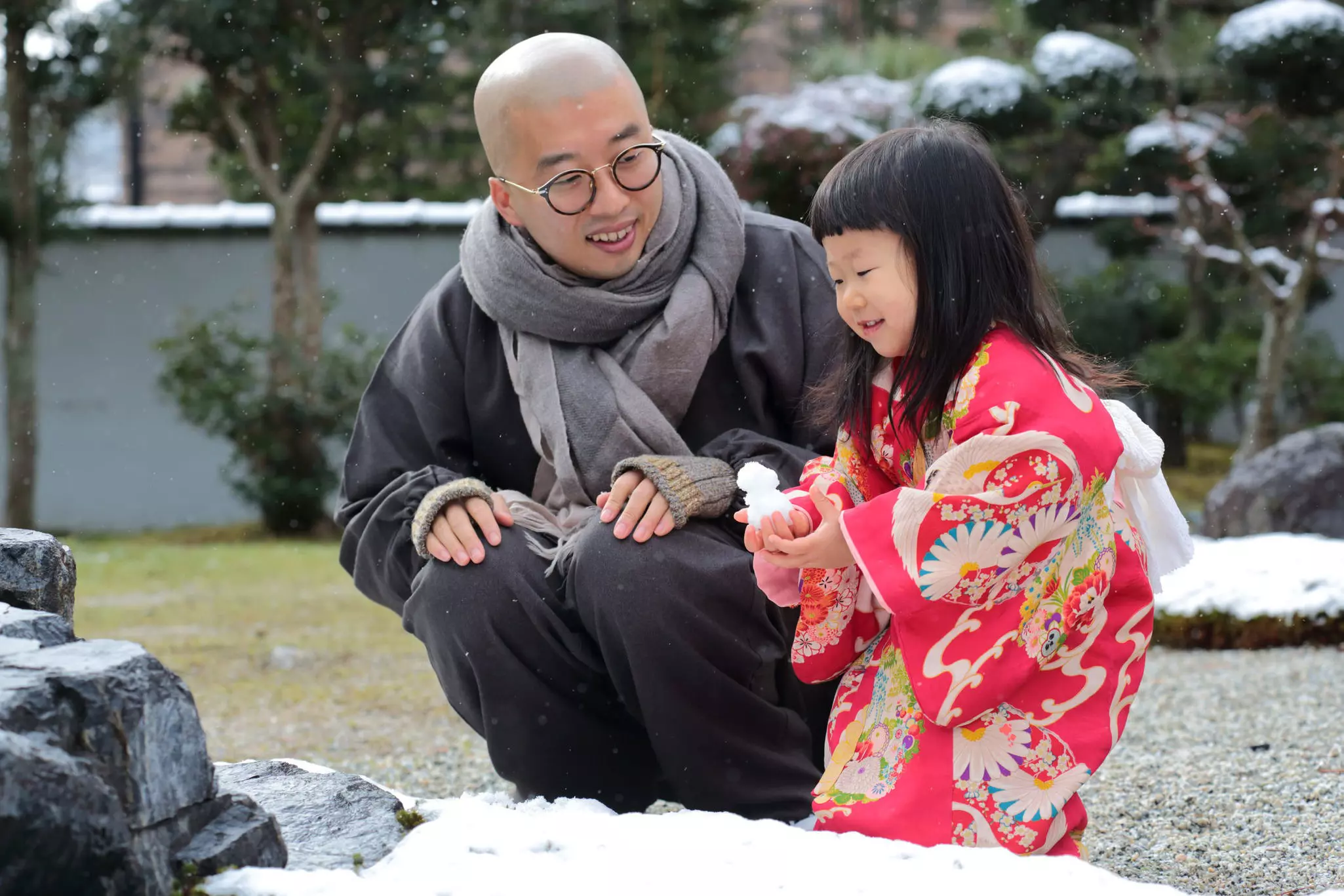 Father and his two-year-old daughter wearing kimonos and playing with snow at a garden in Kyoto.
