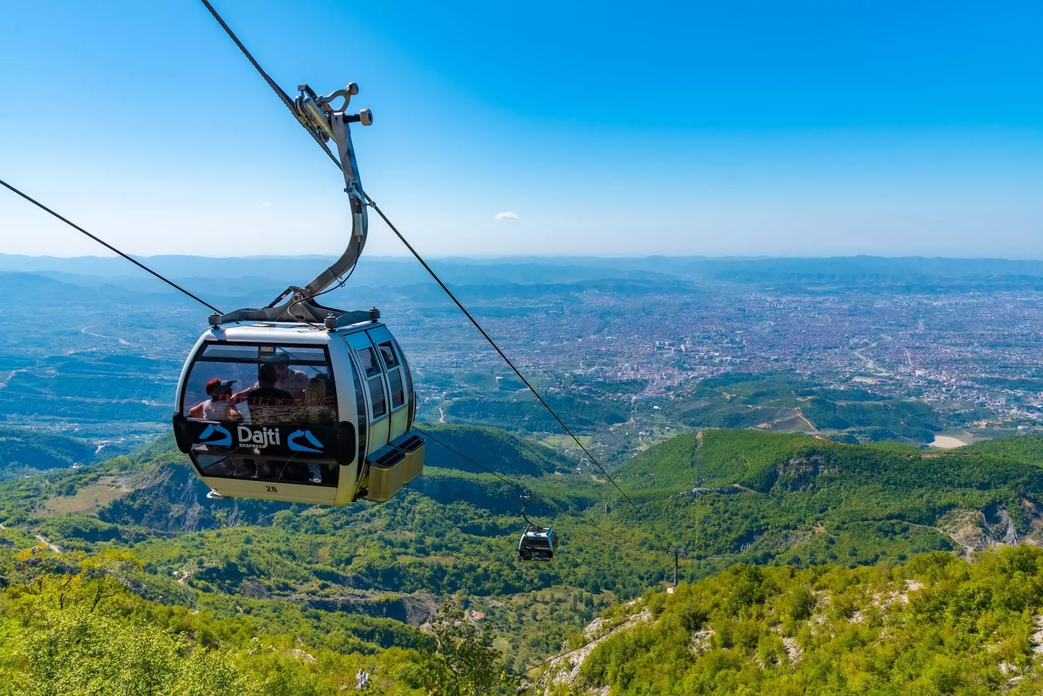 A cable car over green hills with an Albanian city in the distance.