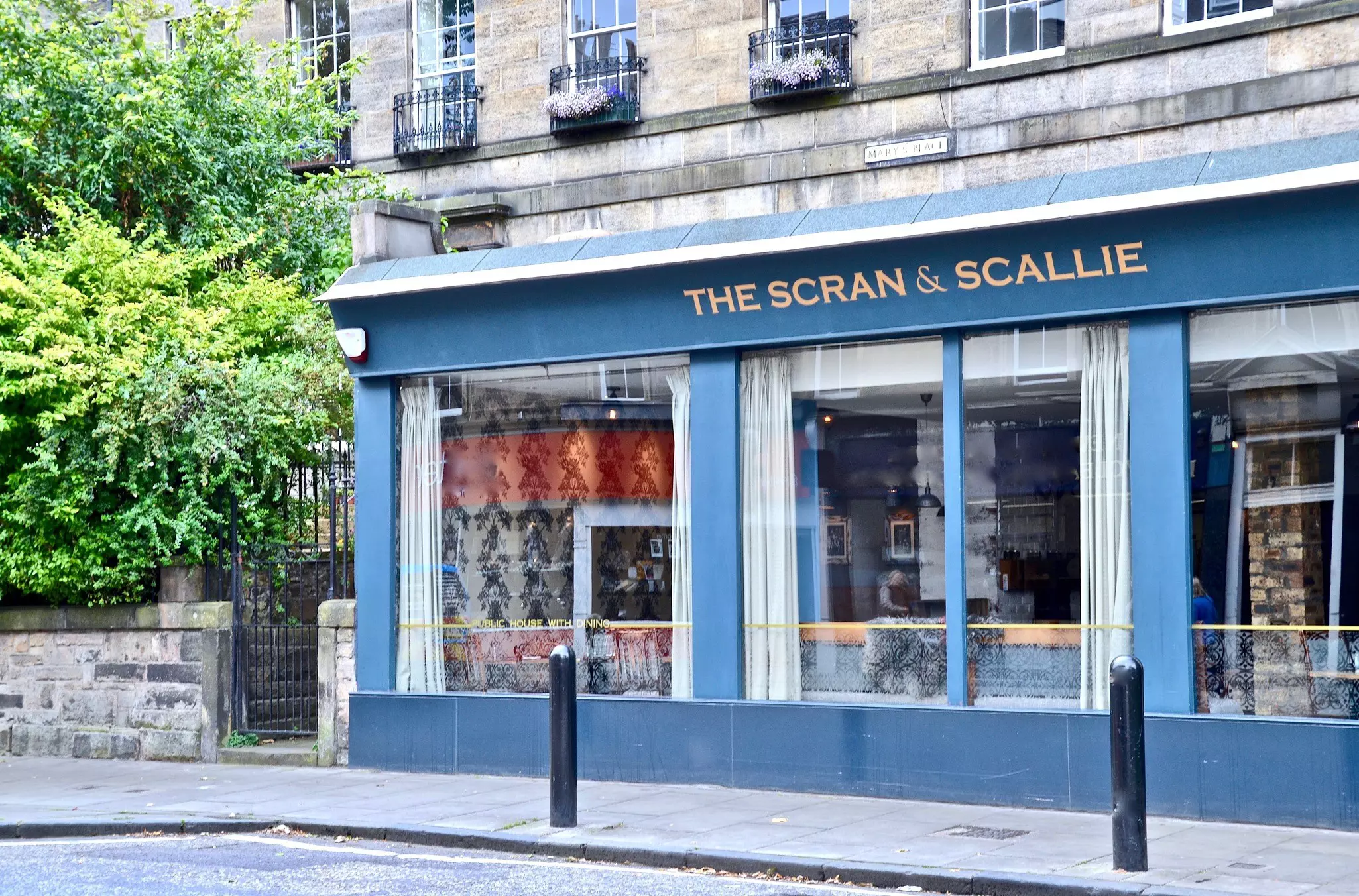A close-up of ham, egg and chips served on a wooden cutting board. The egg is still in a miniature steel frying pan and the chips are in a small tin bucket.