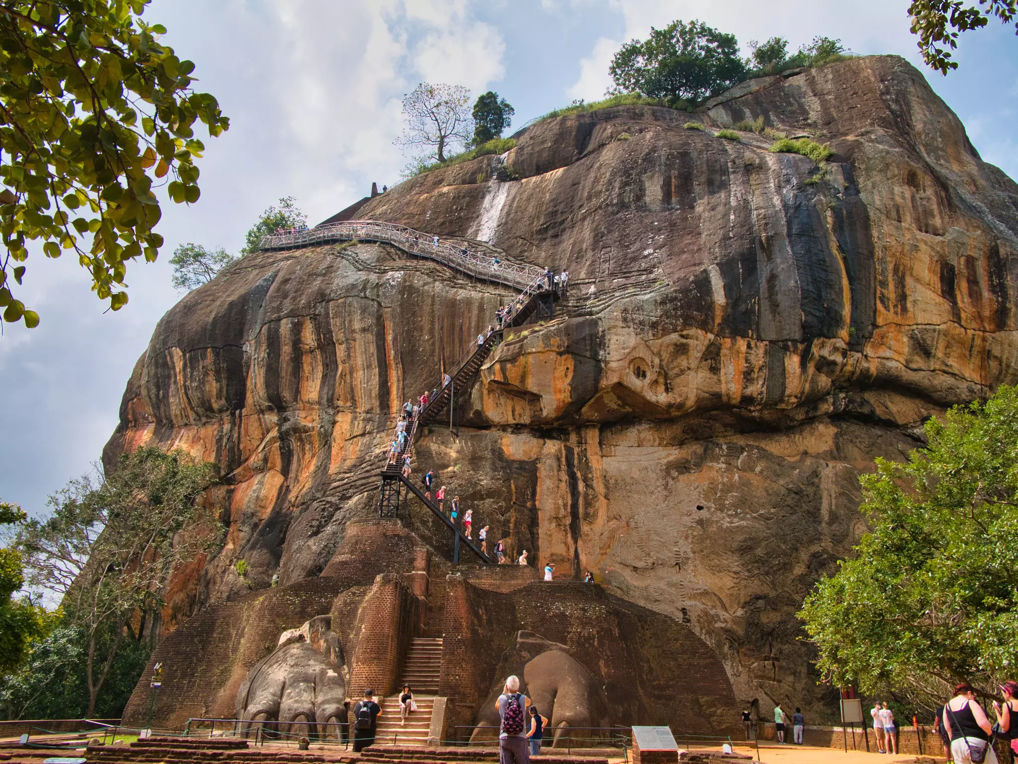 A wide shot of people climbing staircases along the sheer face of a rocky outcrop.