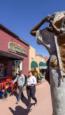 An outdoor sculpture of a child on an adult's back is installed on a sidewalk in front of stores.