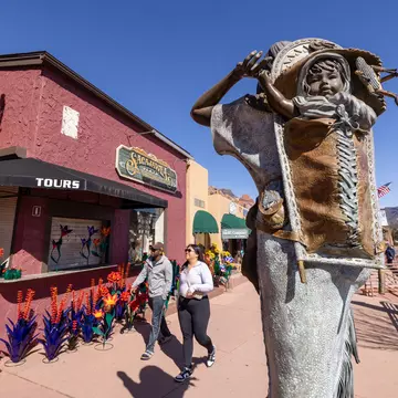 An outdoor sculpture of a child on an adult's back is installed on a sidewalk in front of stores.
