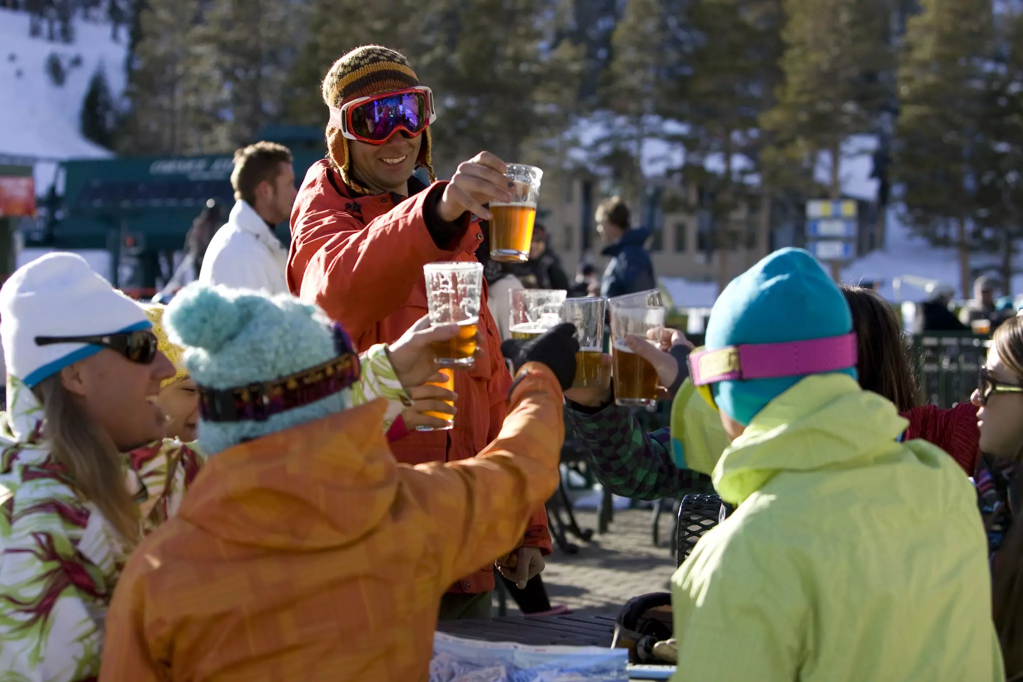 Friends in ski gear socialize and enjoy a beer on the deck on a sunny day on the mountain.