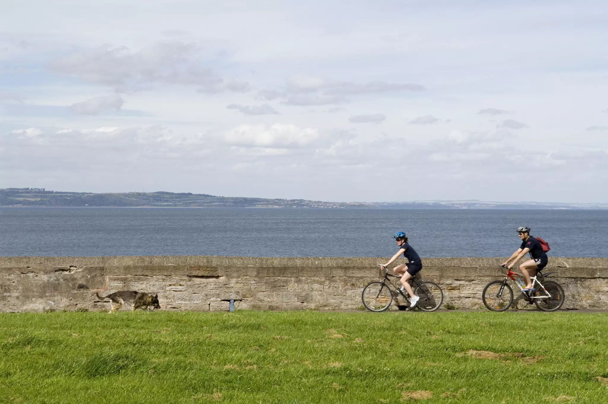 Two cyclists ride their bikes along a path near a body of water