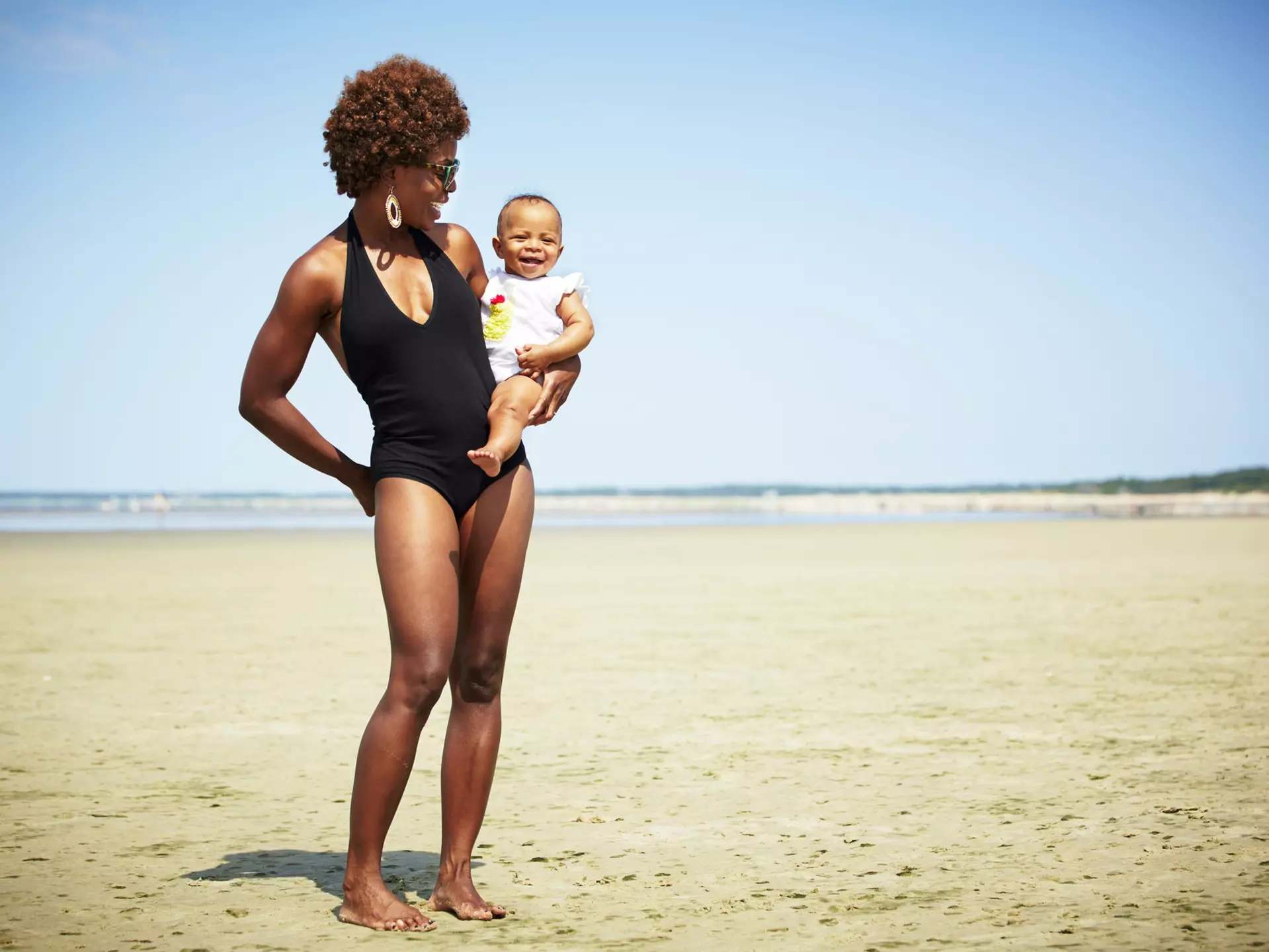 Smiling black mother holding baby girl on an empty beach in Massachusetts where the tide is out