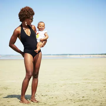 Smiling black mother holding baby girl on an empty beach in Massachusetts where the tide is out