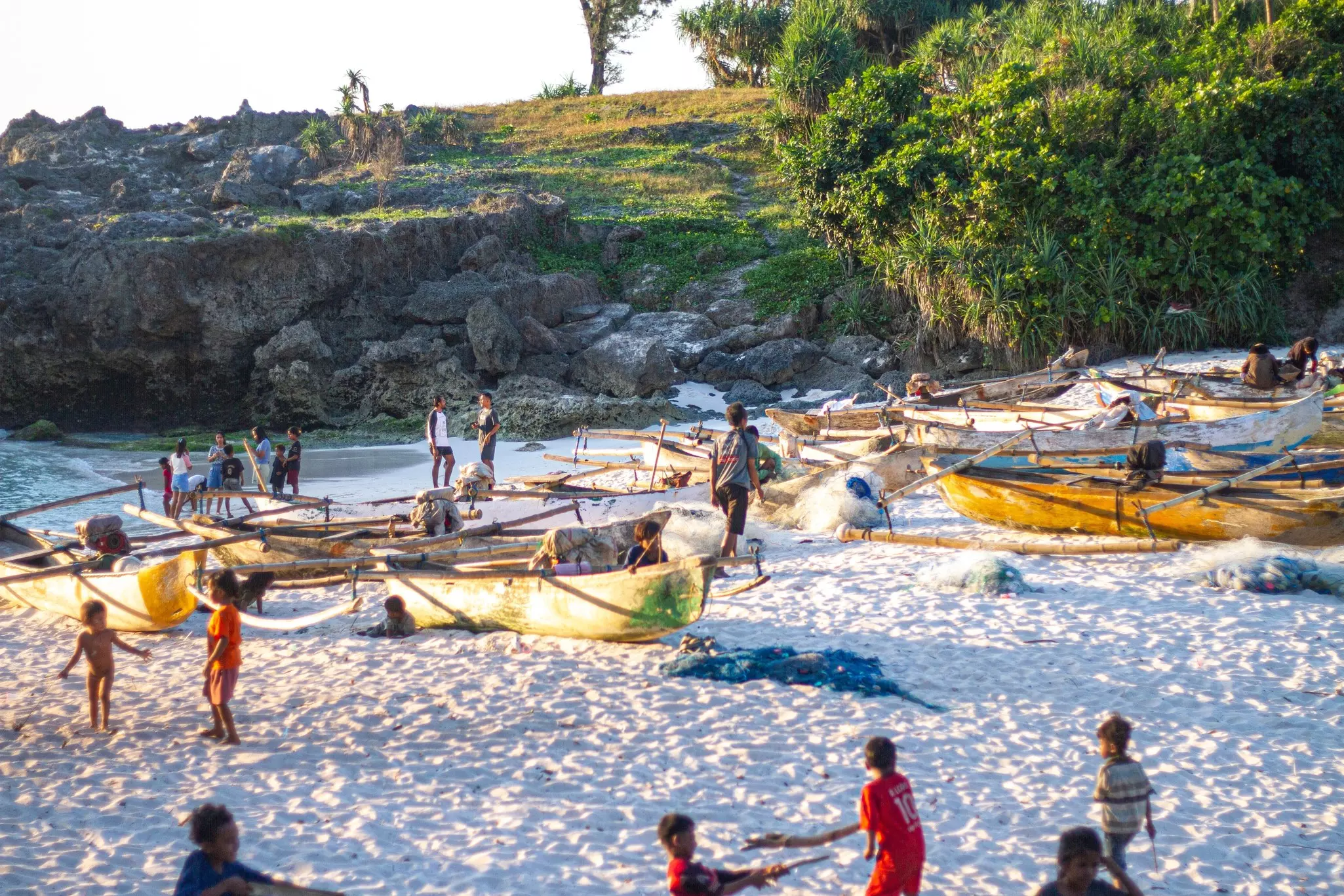 Children play among yellow boats on a white-sand beach in a tropical locale.