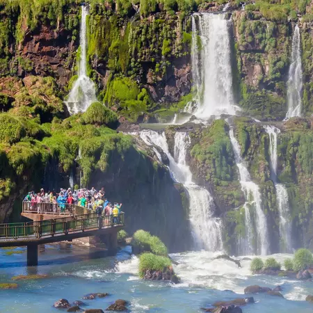 People stand on a platform at the base of a large series of waterfalls.
