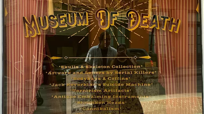 Chamidae and Dylan stand in the reflection of the Museum of Death sign. 