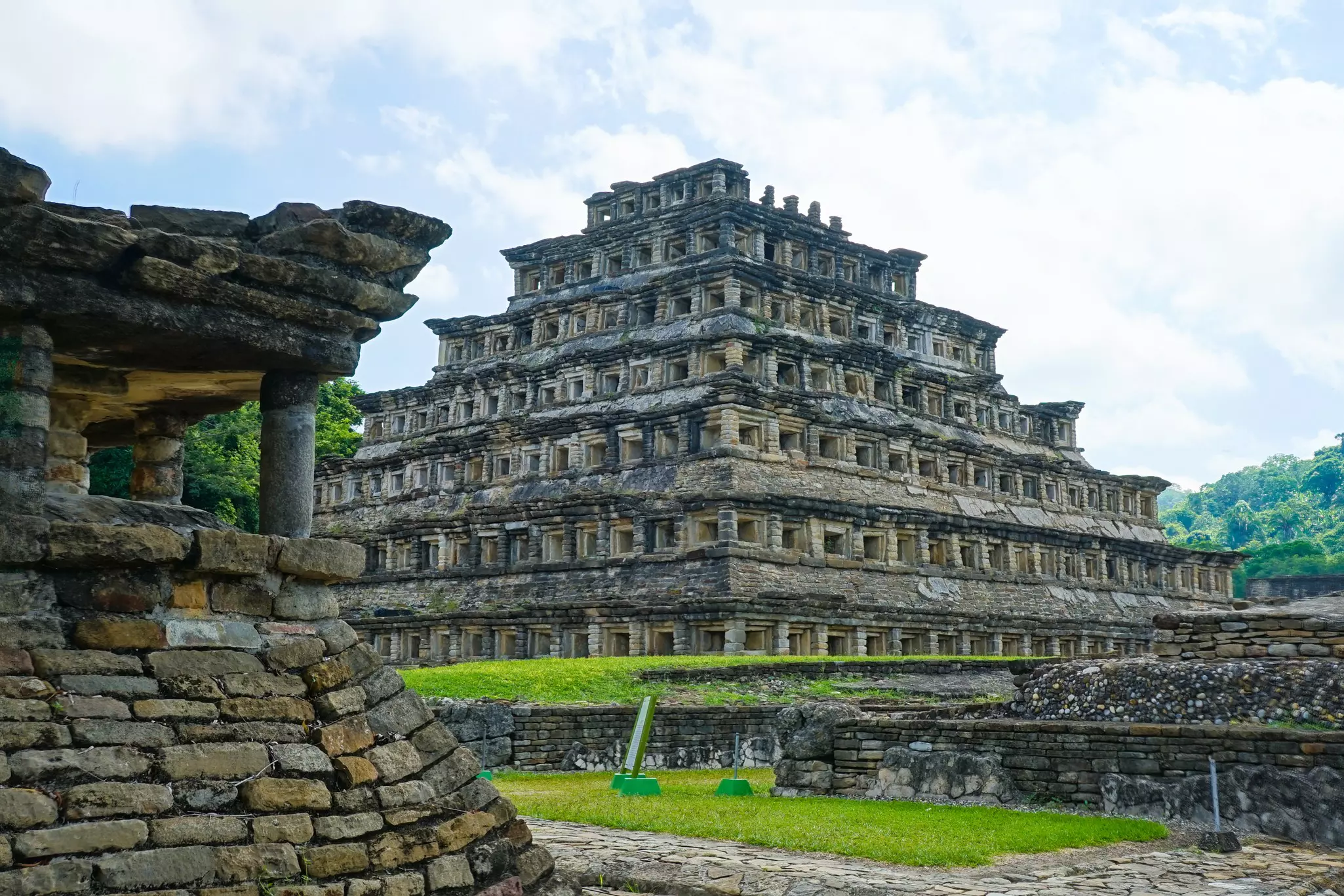 Historic, multilevel stone ruins in good condition surrounded by green grass and cobbled pathways on a mostly sunny day.