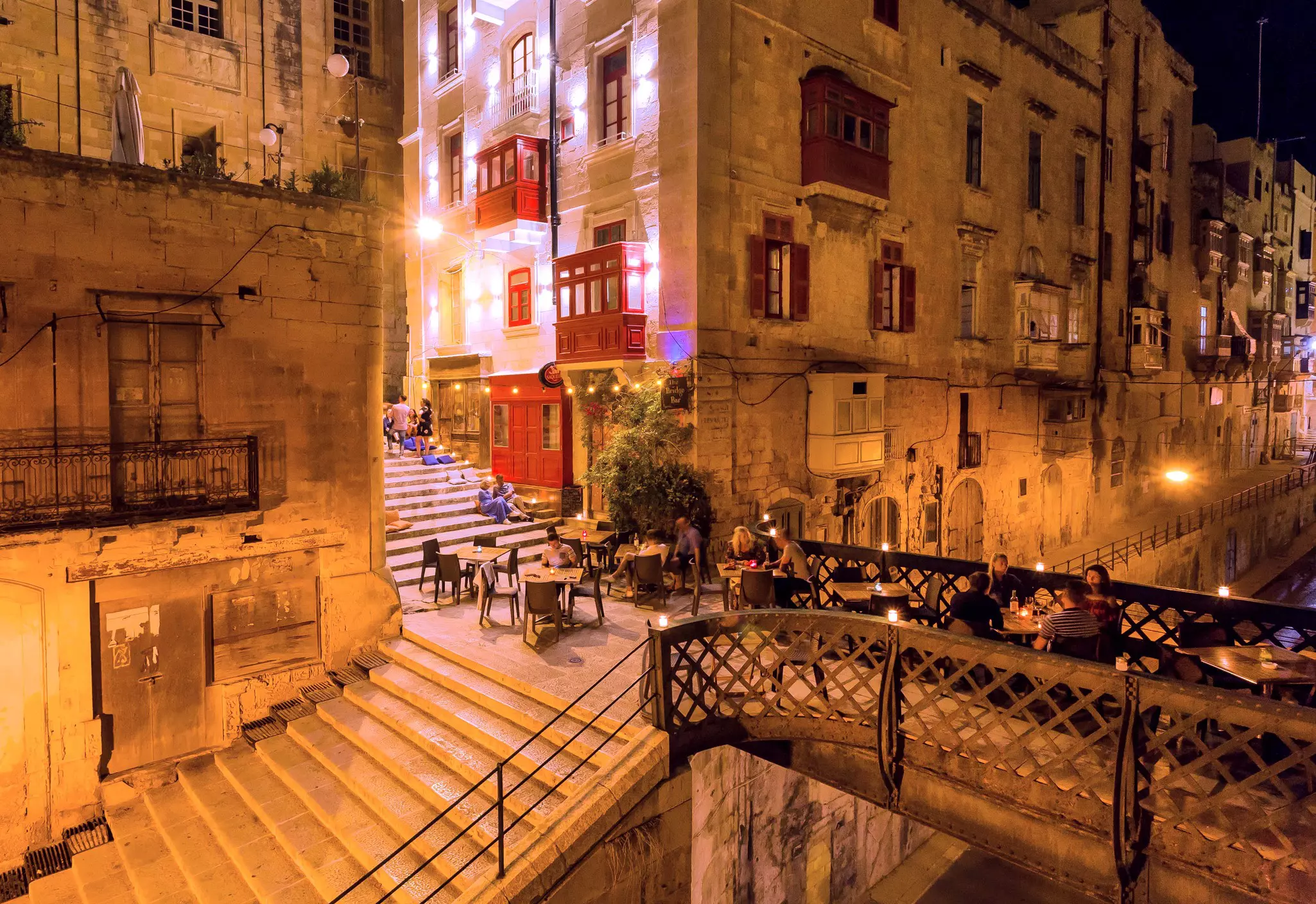 A series of tables laid out on a stone bridge between tall buildings. People drink wine at the tables.