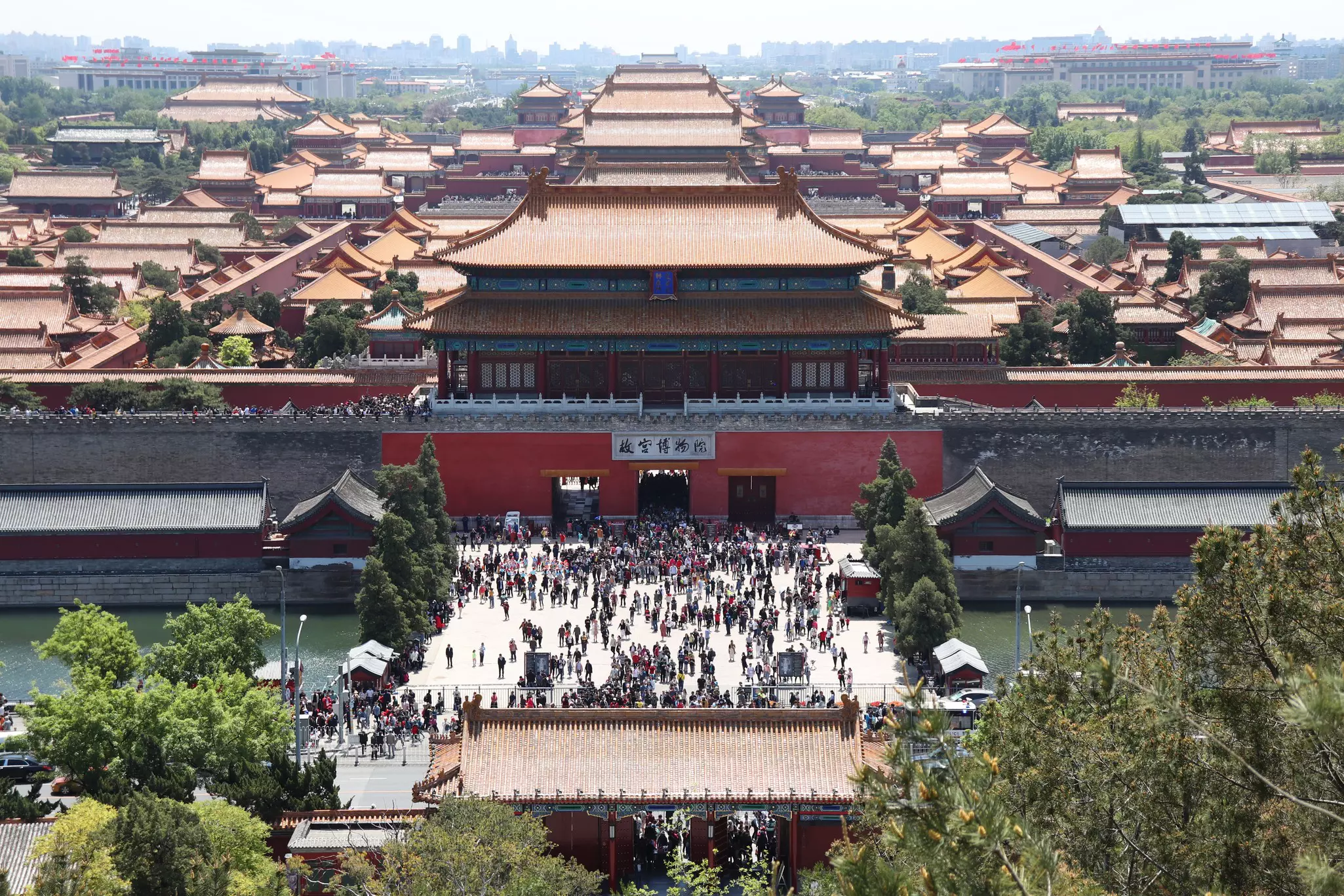 A vast complex of large ancient buildings surrounded by walls with people in an open courtyard near the entrance.