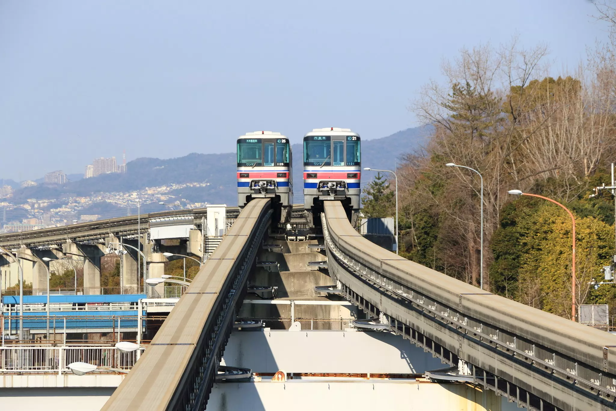 Two monorail trains are seen head-on traveling down two elevated tracks through a densely populated area.