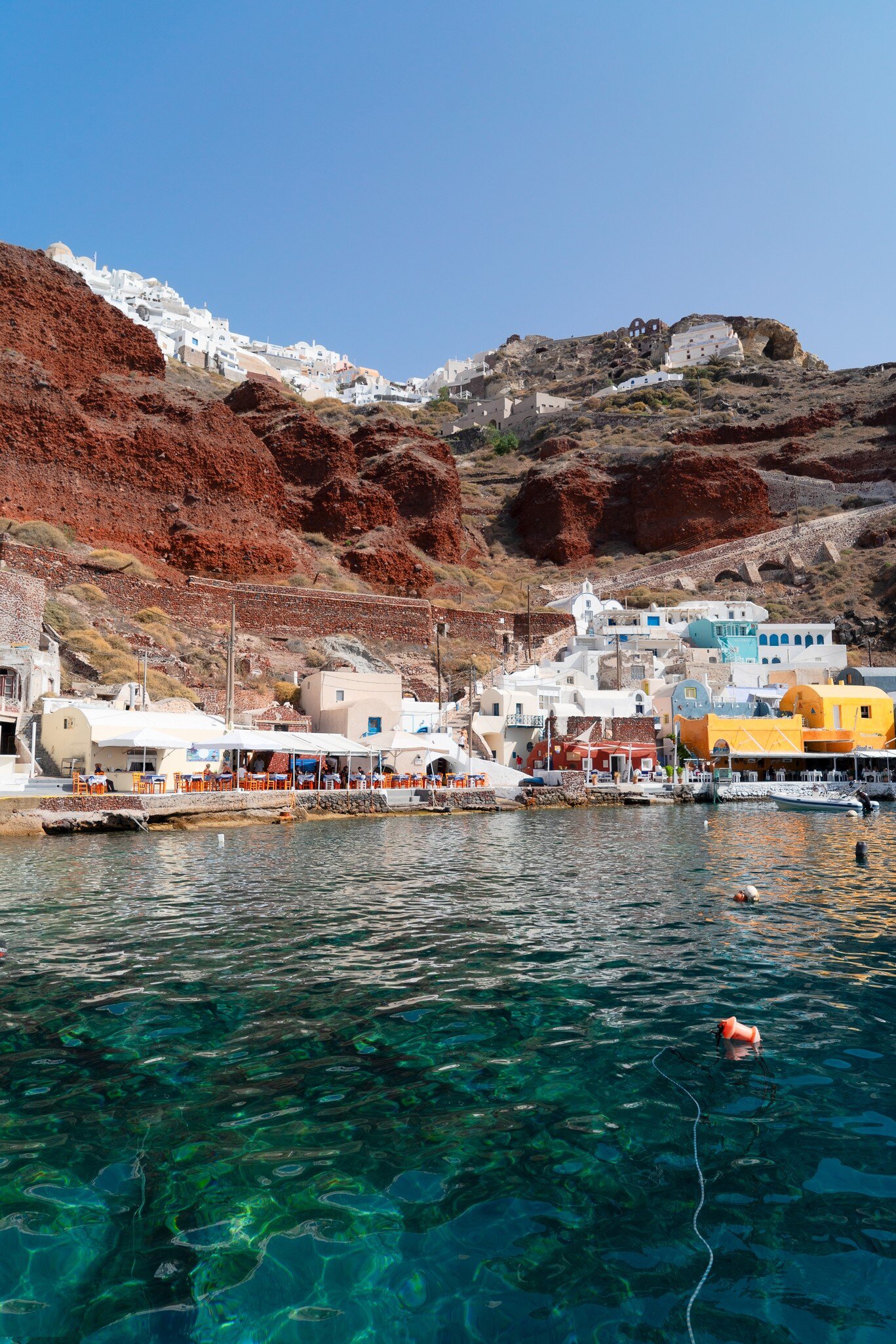 The vibrant Amoudi Bay with boats docked in the crystal clear water at the port of Oia in Santorini during summer.