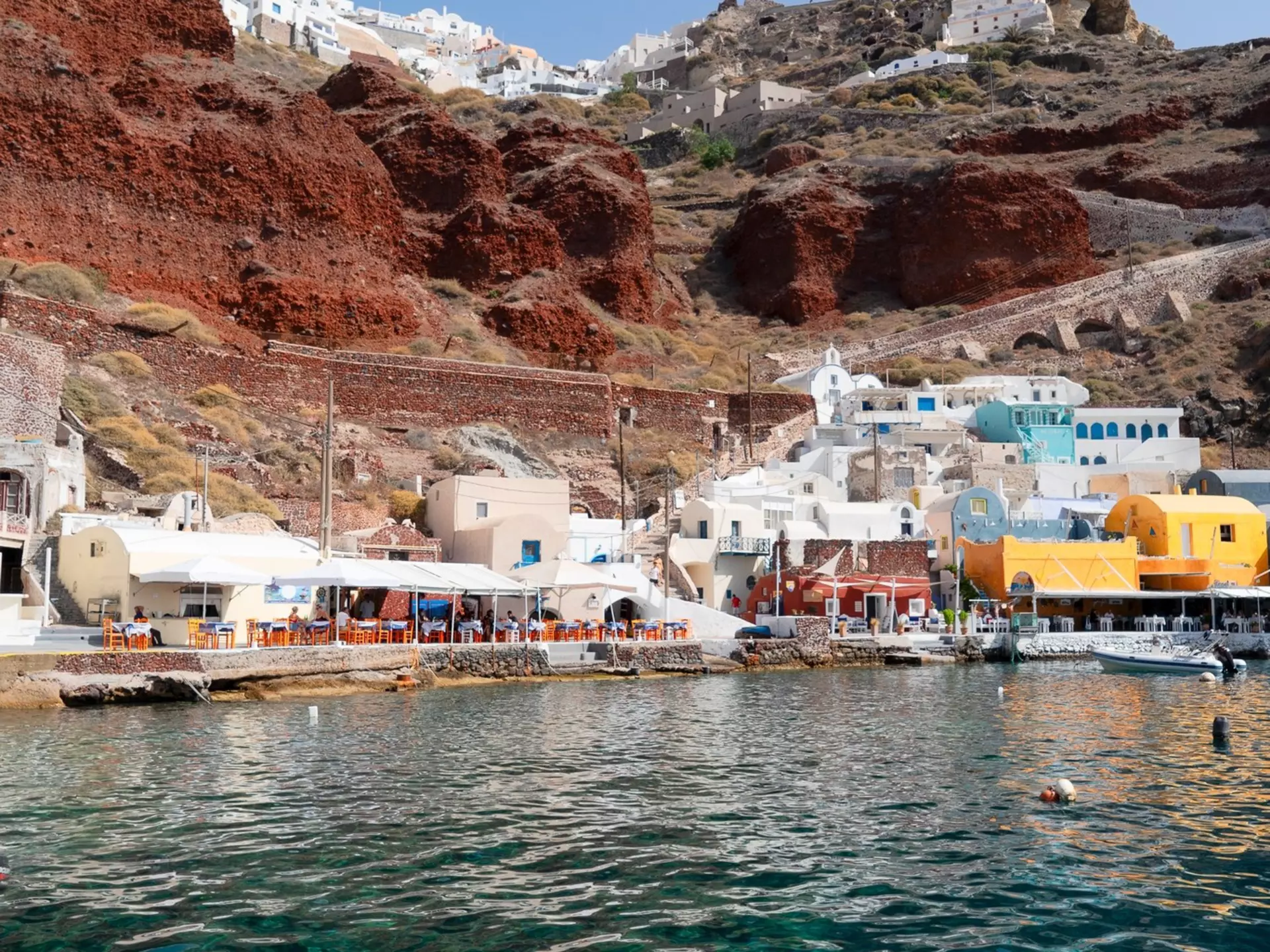 The vibrant Amoudi Bay with boats docked in the crystal clear water at the port of Oia in Santorini during summer.