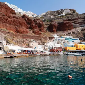 The vibrant Amoudi Bay with boats docked in the crystal clear water at the port of Oia in Santorini during summer.