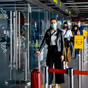 Passengers wearing N95 face masks waiting in line at airport terminal