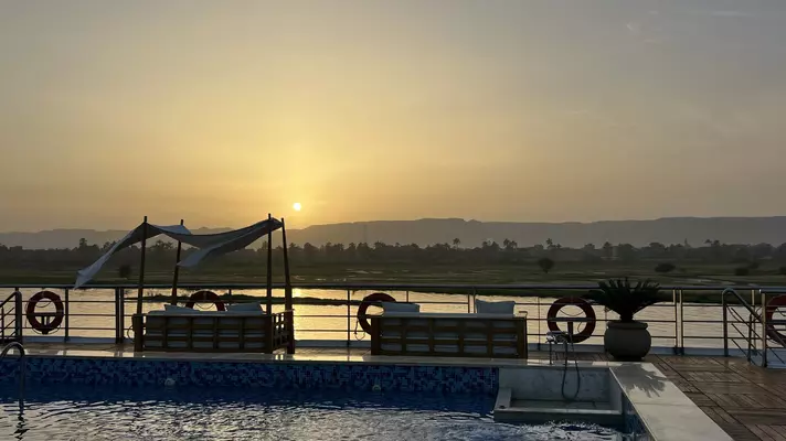 A pool lined with large couches in front of a river of water