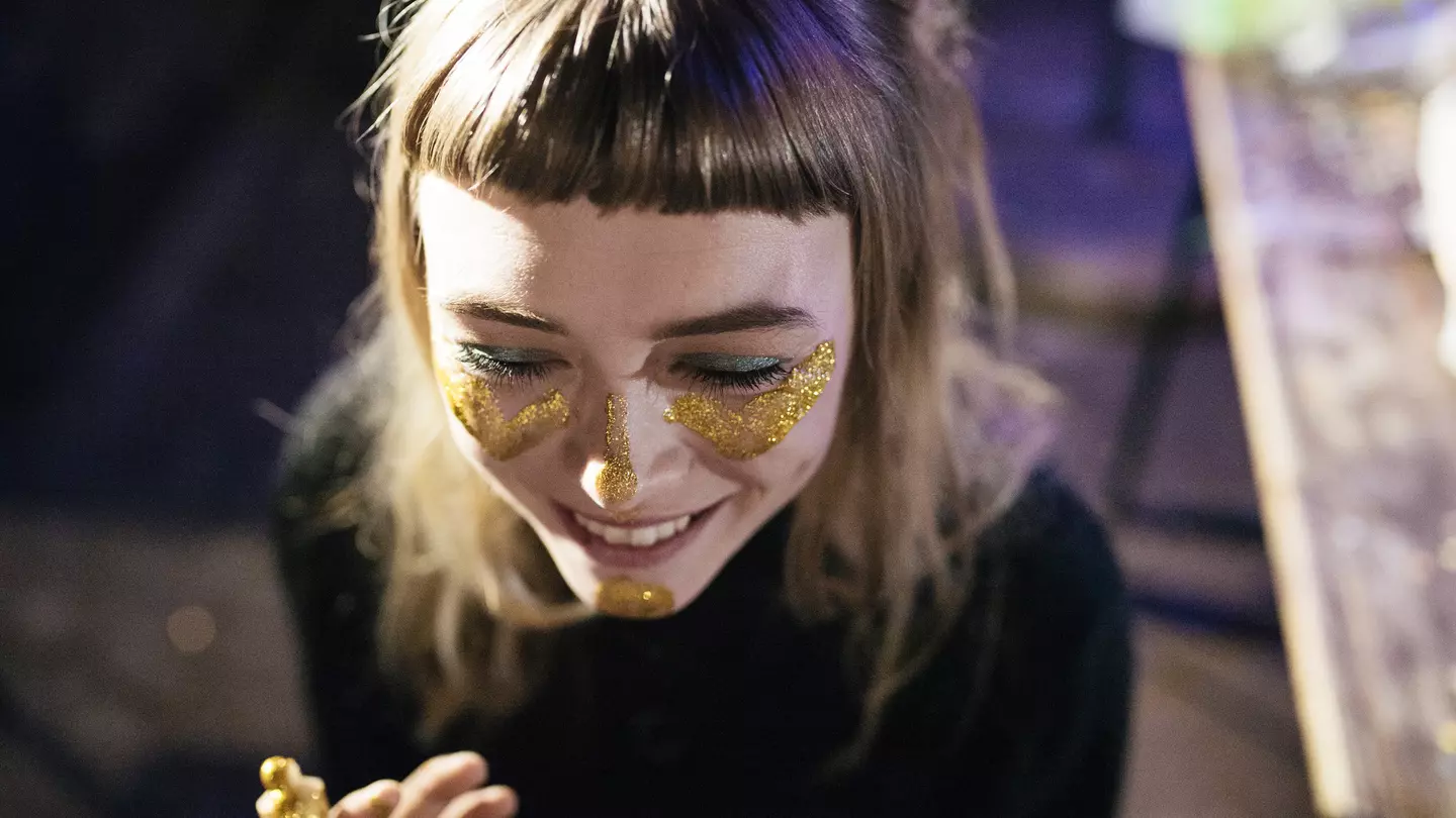 A woman smiles as she paints her face with gold glitter while out clubbing