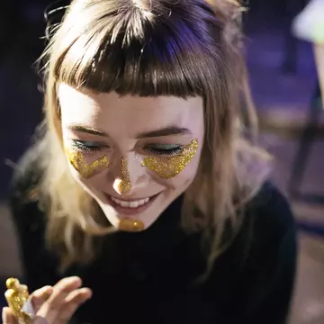 A woman smiles as she paints her face with gold glitter while out clubbing