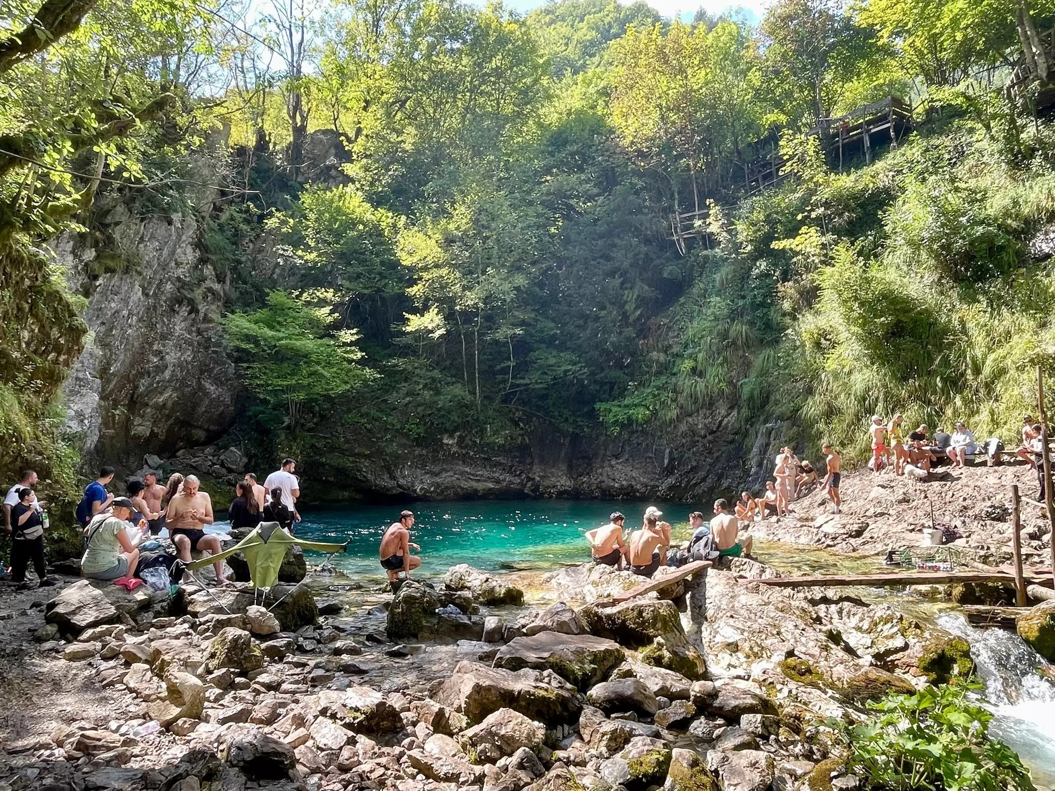 People chill out beside a waterhole deep in woodland on a sunny day.
