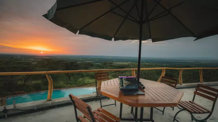 An outside table and chairs with an umbrella on a terrace overlooking a pool and a vast expanse of grassland