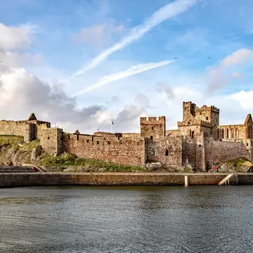 Ruined sandstone walls and towers of Peel Castle on St Patrick's Isle above calm water in Peel, Isle of Man