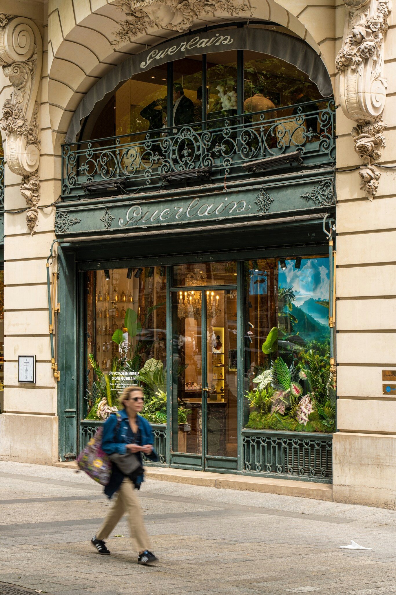 Guerlain boutique with tropical decorations on the Champs Élysées in Paris as a woman walks past.