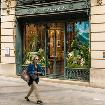 Guerlain boutique with tropical decorations on the Champs Élysées in Paris as a woman walks past.