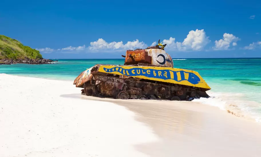 Rusted tank painted with the word Culebra sits on white sand at the water's edge, Culebra, Puerto Rico